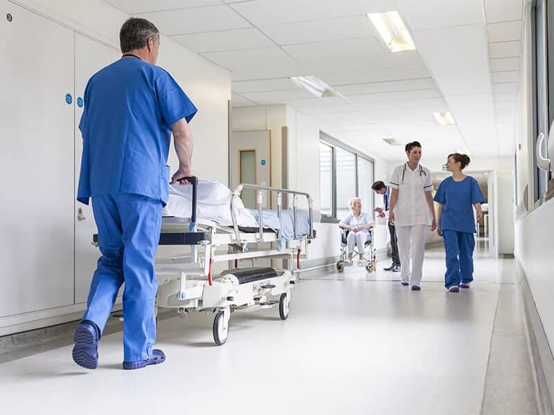 A nurse wheels an empty gurney down a hospital hallway
